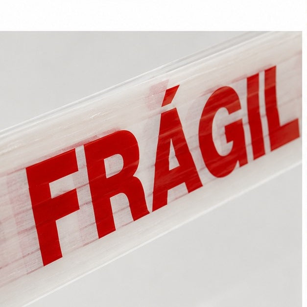 Close-up da impressão FRÁGIL em fita adesiva — texto em destaque vermelho sobre filme branco