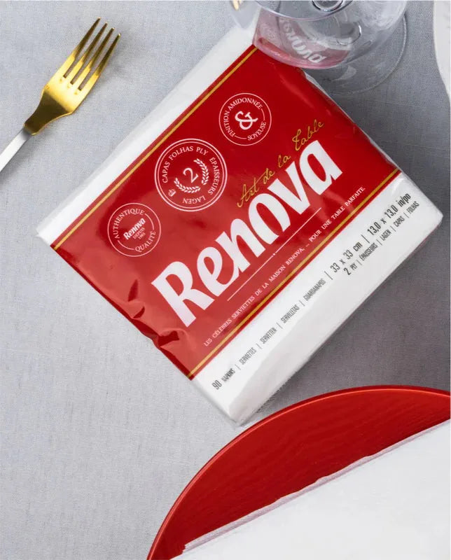 Pacote de guardanapos brancos Renova Art de La Table numa mesa com garfo dourado e prato vermelho