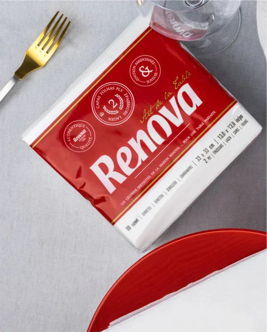 Pacote de guardanapos brancos Renova Art de La Table numa mesa com garfo dourado e prato vermelho